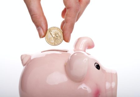a hand holding a small piggy bank with a coin and a coin