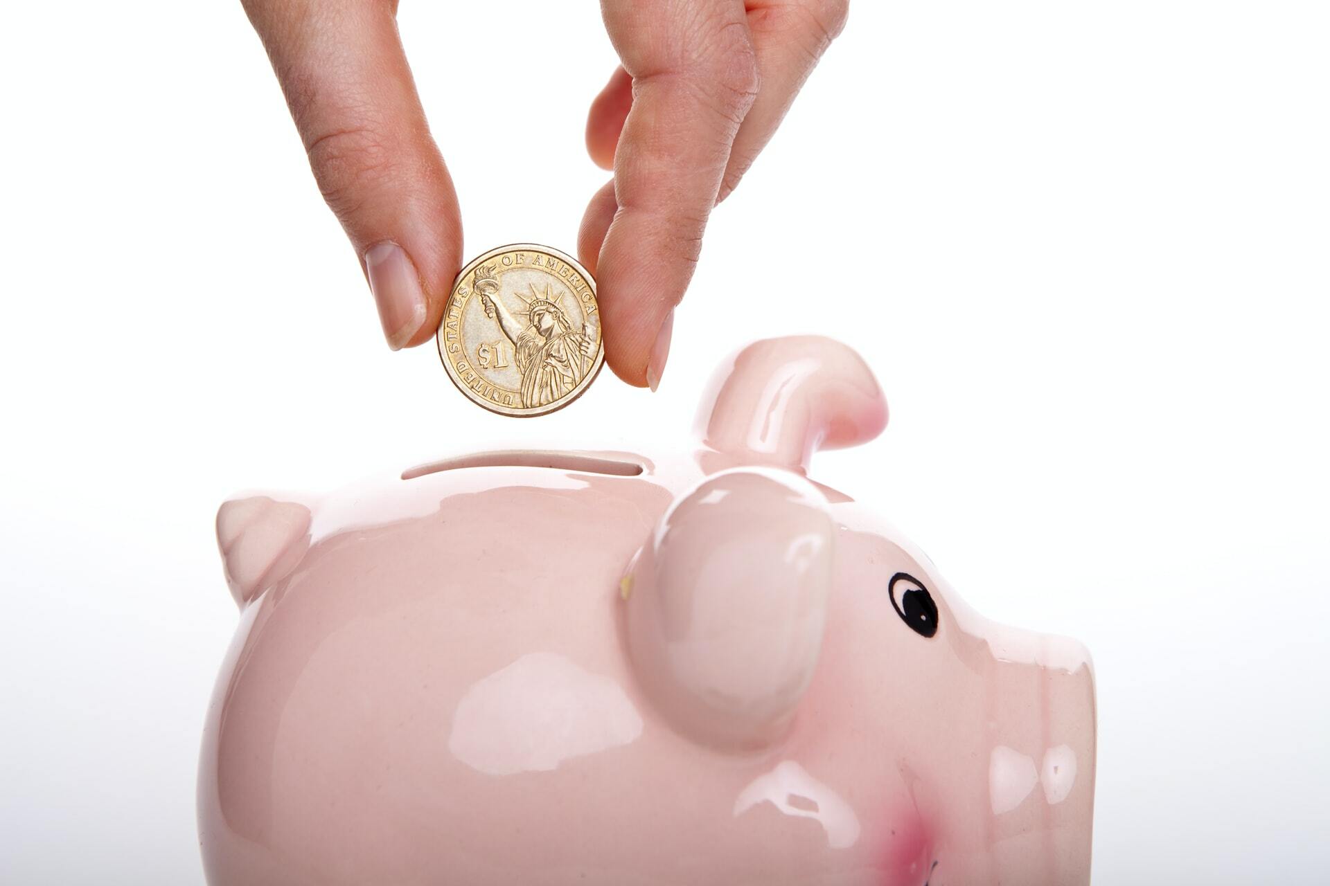 a hand holding a small piggy bank with a coin and a coin