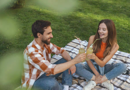 a man and woman sitting on a blanket in a grassy field